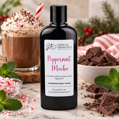 A bottle of Jarhead Aromatics Peppermint Mocha Handmade Body Wash stands on a marble surface surrounded by a cup of hot cocoa, chopped chocolate, and fresh mint leaves.