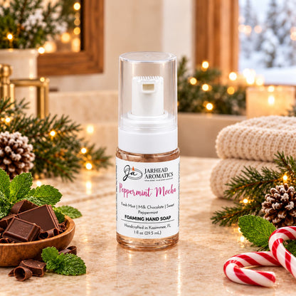 A bottle of Peppermint Mocha Handmade Foaming Hand Soap | Chocolate Mint & Vanilla on a counter, surrounded by chocolate squares, fresh mint leaves, and a candy cane.