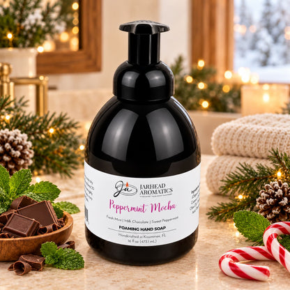 A bottle of Peppermint Mocha Handmade Foaming Hand Soap | Chocolate Mint & Vanilla sitting on a counter next to chocolate squares, fresh mint, and a candy cane.