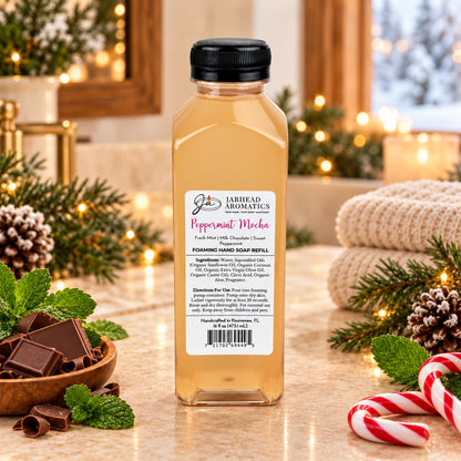 A clear plastic bottle of Jarhead Aromatics Peppermint Mocha Handmade Foaming Hand Soap surrounded by chocolate squares, mint leaves, and a candy cane.