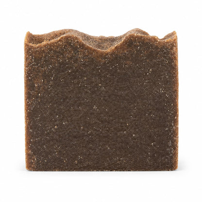 A rectangular bar of Jarhead Aromatics Pine Tar Handmade Natural Artisan Soap, featuring a rough, textured surface and an uneven, wavy top edge, is displayed against a plain white background.