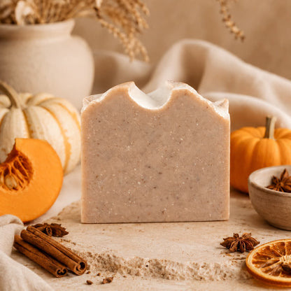 A bar of Pumpkin + Spice Handmade Artisan Soap by Jarhead Aromatics rests on a stone surface, surrounded by pumpkins, cinnamon sticks, star anise, and neutral pottery, creating a cozy autumn ambiance with its inviting spiced pumpkin exfoliating scent.
