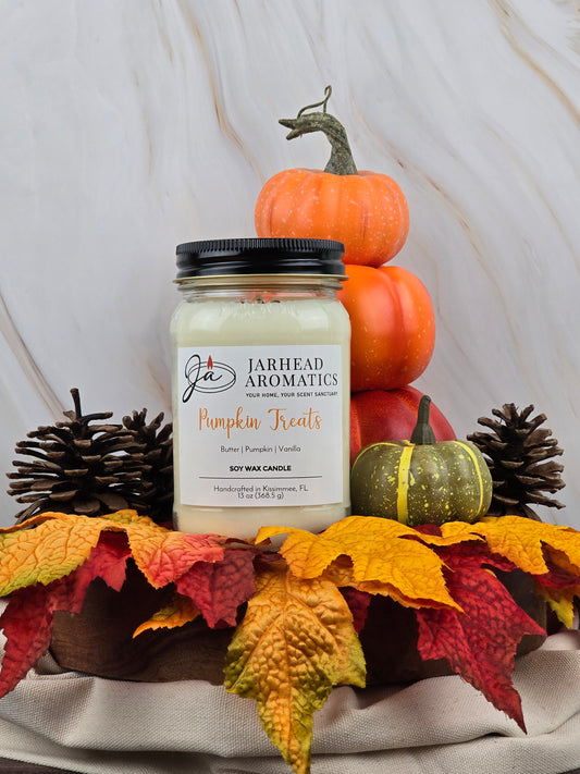 A Jarhead Aromatics Pumpkin Treats - Soy Wax Candle with rich caramel essence rests on a cloth embellished with autumn leaves, pinecones, and pumpkins. The wooden background enhances the autumn atmosphere.