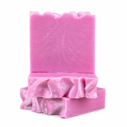 Two vibrant pink Rose + Hibiscus Handmade Coconut Milk Artisan Soap bars by Jarhead Aromatics stand out—one displayed upright, with two more stacked flat beneath it. These romantic floral soaps feature wavy, textured tops and marbled white streaks along the sides.