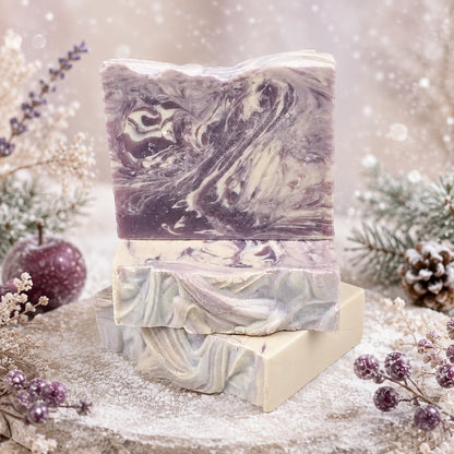 Three rectangular bars of swirled purple and white Sugar Plum Handmade Coconut Milk Artisan Soap stacked on a stone surface.