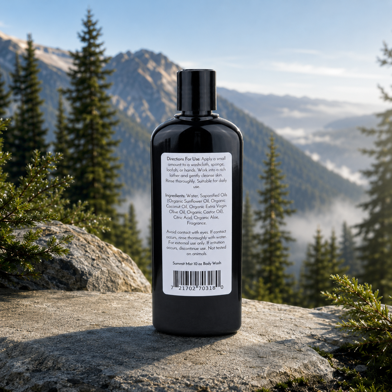 A black bottle of Jarhead Aromatics Summit Mist Handmade Body Wash with organic aloe and plant-based oils sits on a log outdoors. Its white label displays directions, ingredients, and a barcode amid pine trees and distant mountains.