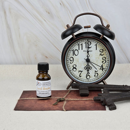 A vintage alarm clock, Jarhead Aromatics Sweet Bourbon Cold Air Diffuser Refill, large old-fashioned keys, and a brown string-tied envelope are displayed on a light surface against a marble background.