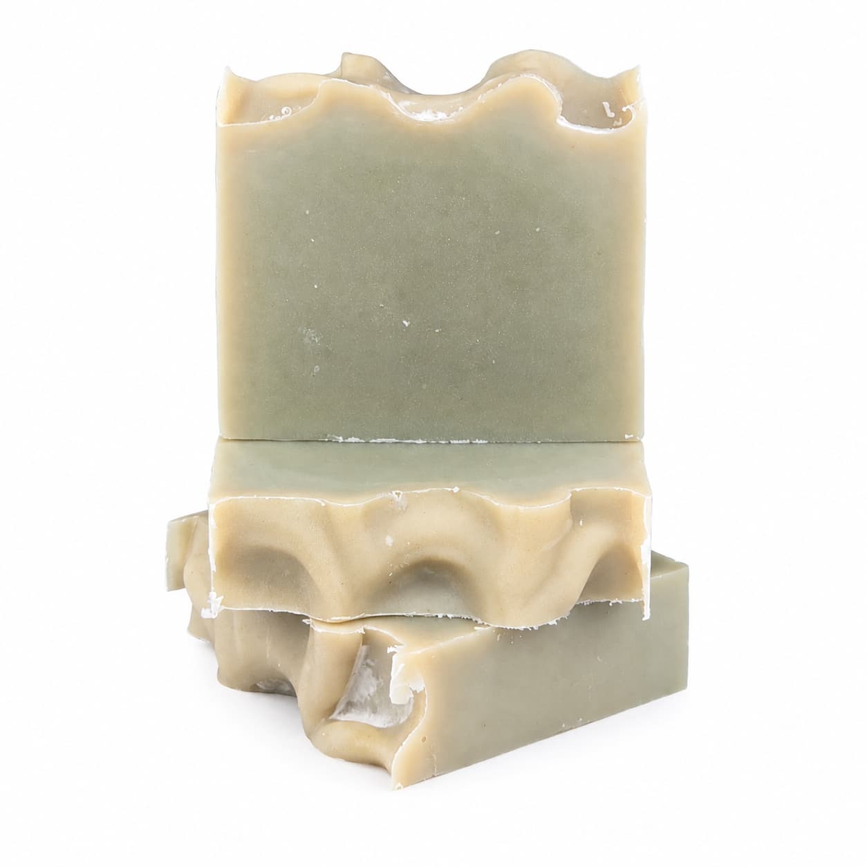 Three stacked bars of Jarhead Aromatics’ Tea Tree Handmade Natural Goat Milk Artisan Soap, featuring uneven, wavy tops and a greenish-beige hue, are arranged against a plain white background. These Fresh Herbal Tea Tree Goat Milk Soaps embody both natural elegance and the gentle care of handcrafted quality.