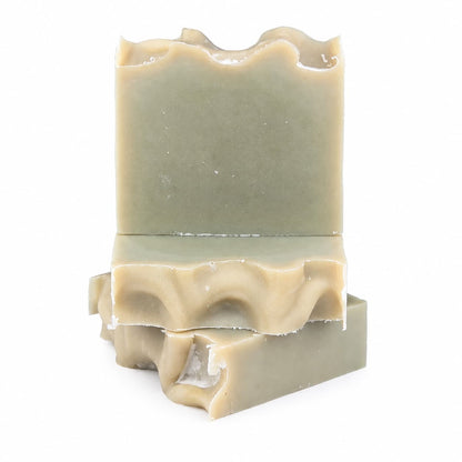 Three stacked bars of Jarhead Aromatics’ Tea Tree Handmade Natural Goat Milk Artisan Soap, featuring uneven, wavy tops and a greenish-beige hue, are arranged against a plain white background. These Fresh Herbal Tea Tree Goat Milk Soaps embody both natural elegance and the gentle care of handcrafted quality.