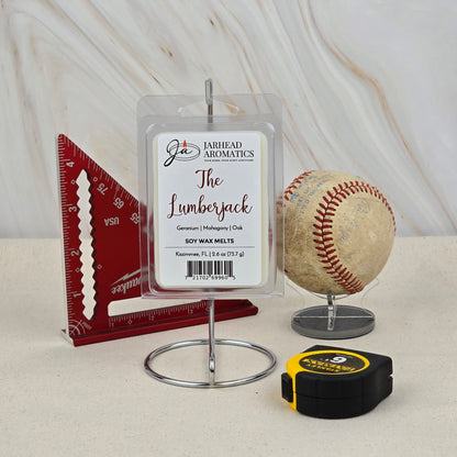 A package of Jarhead Aromatics The Lumberjack Soy Wax Melt | Mahogany Cedar & Oak is shown on a stand with a red ruler, worn baseball, and tape measure—emphasizing its hand-poured soy wax and rugged woodsy scent.