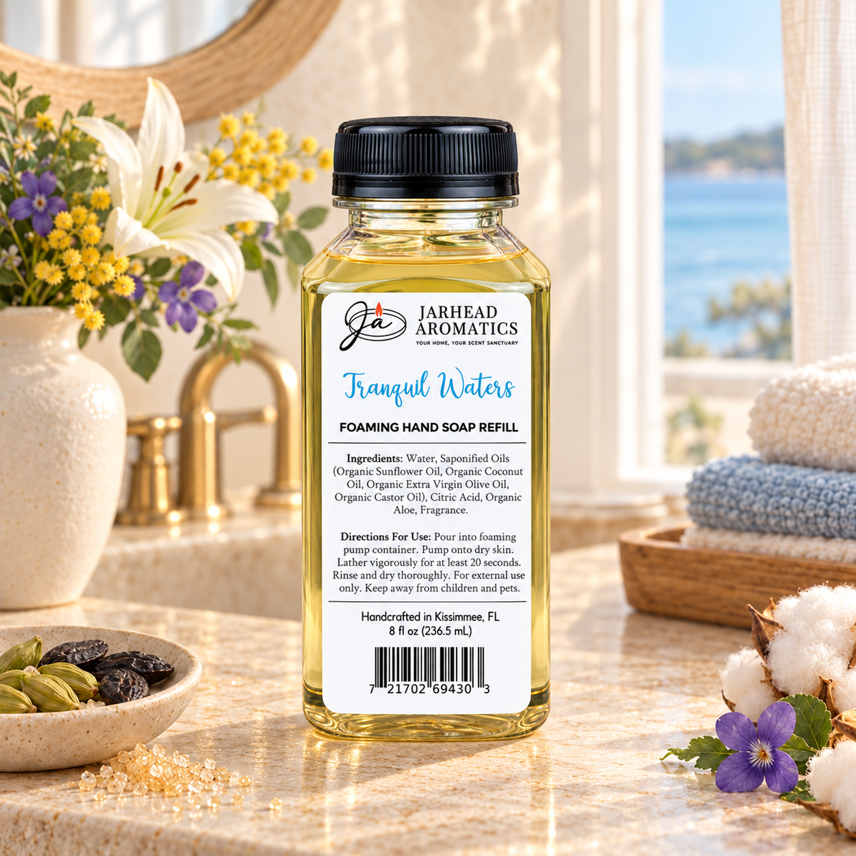 Clear bottle of Tranquil Waters Handmade Foaming Hand Soap | Marine, Lily & Tonka Bean refill with a label listing ingredients and directions, standing on a bathroom counter.