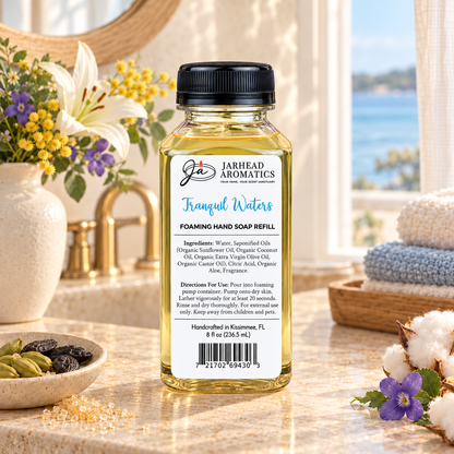 Clear bottle of Tranquil Waters Handmade Foaming Hand Soap | Marine, Lily & Tonka Bean refill with a label listing ingredients and directions, standing on a bathroom counter.