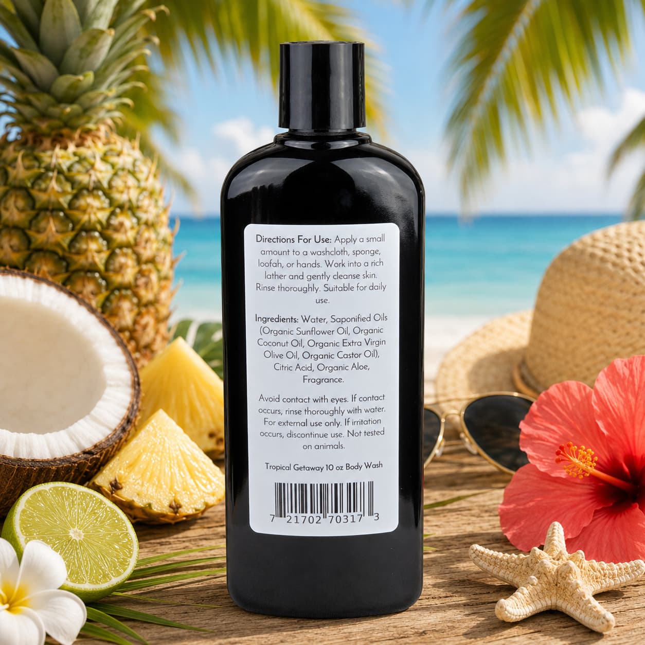 A black bottle of Jarhead Aromatics Tropical Getaway Handmade Body Wash | Moisturizing Body Wash with Organic Aloe & Plant-Based Oils, featuring its labeled packaging, sits on a table by the beach, surrounded by tropical flowers, seashells, and palm leaves, with the ocean and blue sky in the background.