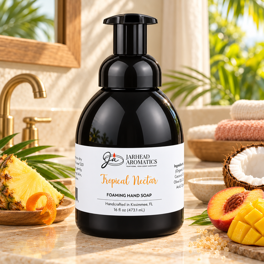 A black bottle of Jarhead Aromatics Tropical Nectar Handmade Foaming Hand Soap | Pineapple, Mango & Coconut Milk with a white label featuring a pineapple, mango, and coconut arrangement on a stone bathroom vanity.