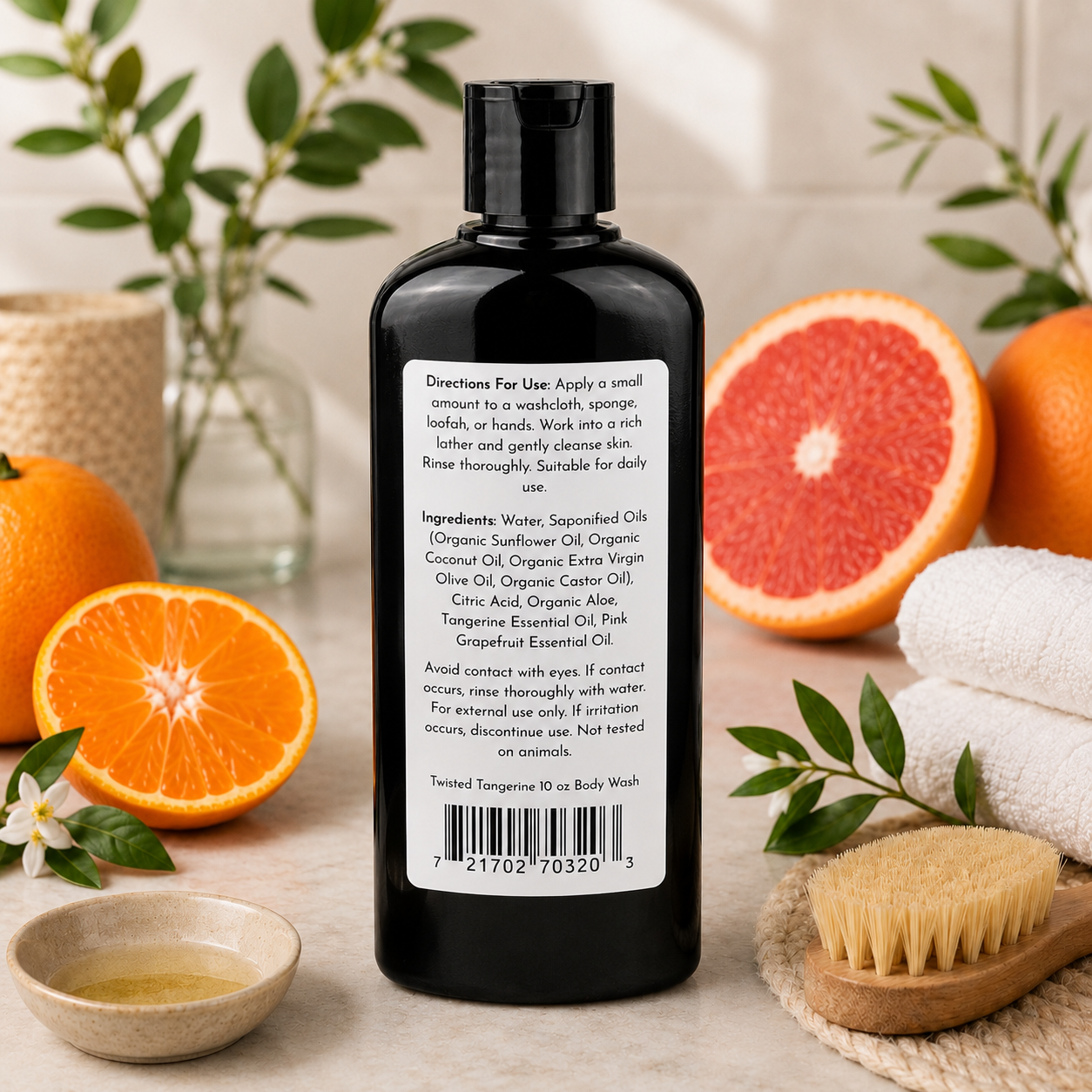 A black bottle of Jarhead Aromatics Twisted Tangerine Handmade Natural Body Wash with a white label is displayed on marble, surrounded by orange slices, a wooden brush, white towel, and greenery in a bright, natural setting.