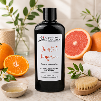 A black bottle of Jarhead Aromatics Twisted Tangerine Handmade Natural Body Wash with organic aloe and plant-based oils sits among fresh oranges, a brush, towel, green leaves, and spa items. Enjoy this moisturizing natural body wash.