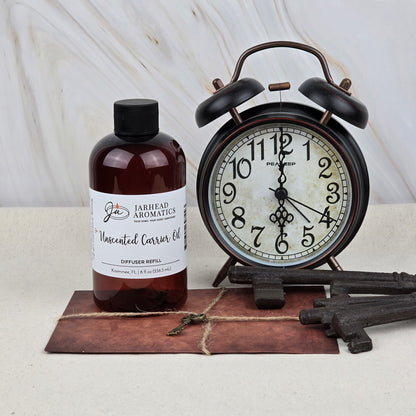A bottle of Jarhead Aromatics Unscented Carrier Oil Diffuser Refill | Base Oil for Reed & Cold Air Diffusers is placed beside a vintage black alarm clock, three antique keys, and a brown envelope on a light marble-background surface.