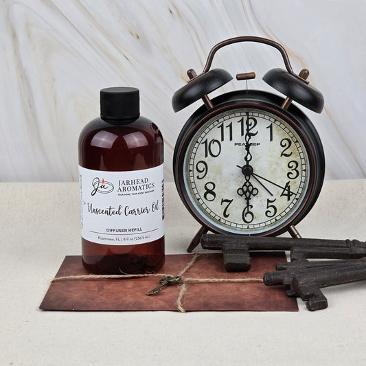 A bottle of Jarhead Aromatics Unscented Carrier Oil Diffuser Refill | Base Oil for Reed & Cold Air Diffusers is placed beside a vintage black alarm clock, three antique keys, and a brown envelope on a light marble-background surface.