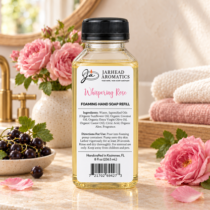 A bottle of Whispering Rose Handmade Foaming Hand Soap | Black Currant, Turkish Rose & White Musk sitting on a counter, surrounded by a bowl of black currants and fresh pink roses.