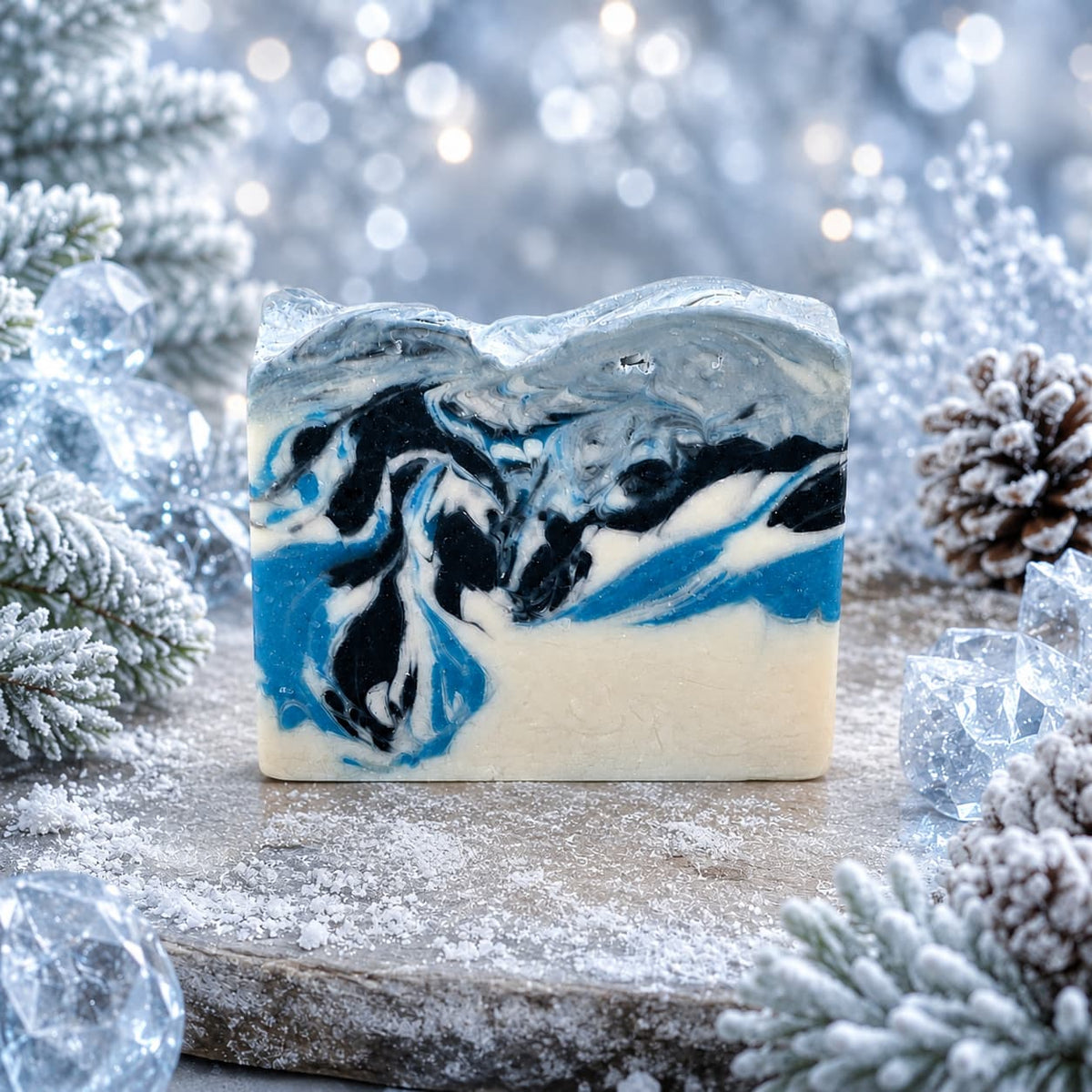 Winter Wonderland Handmade Coconut Milk Artisan Soap with a swirling blue, black, and white marbled pattern, displayed among snowy pine branches and pinecones.