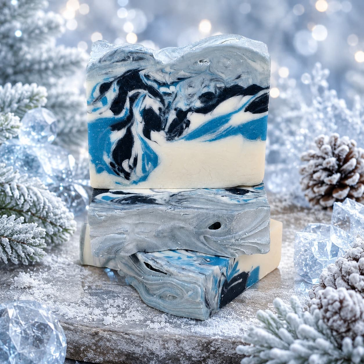 Three bars of Winter Wonderland Handmade Coconut Milk Artisan Soap stacked on a stone surface, featuring swirls of blue, black, white, and silver.