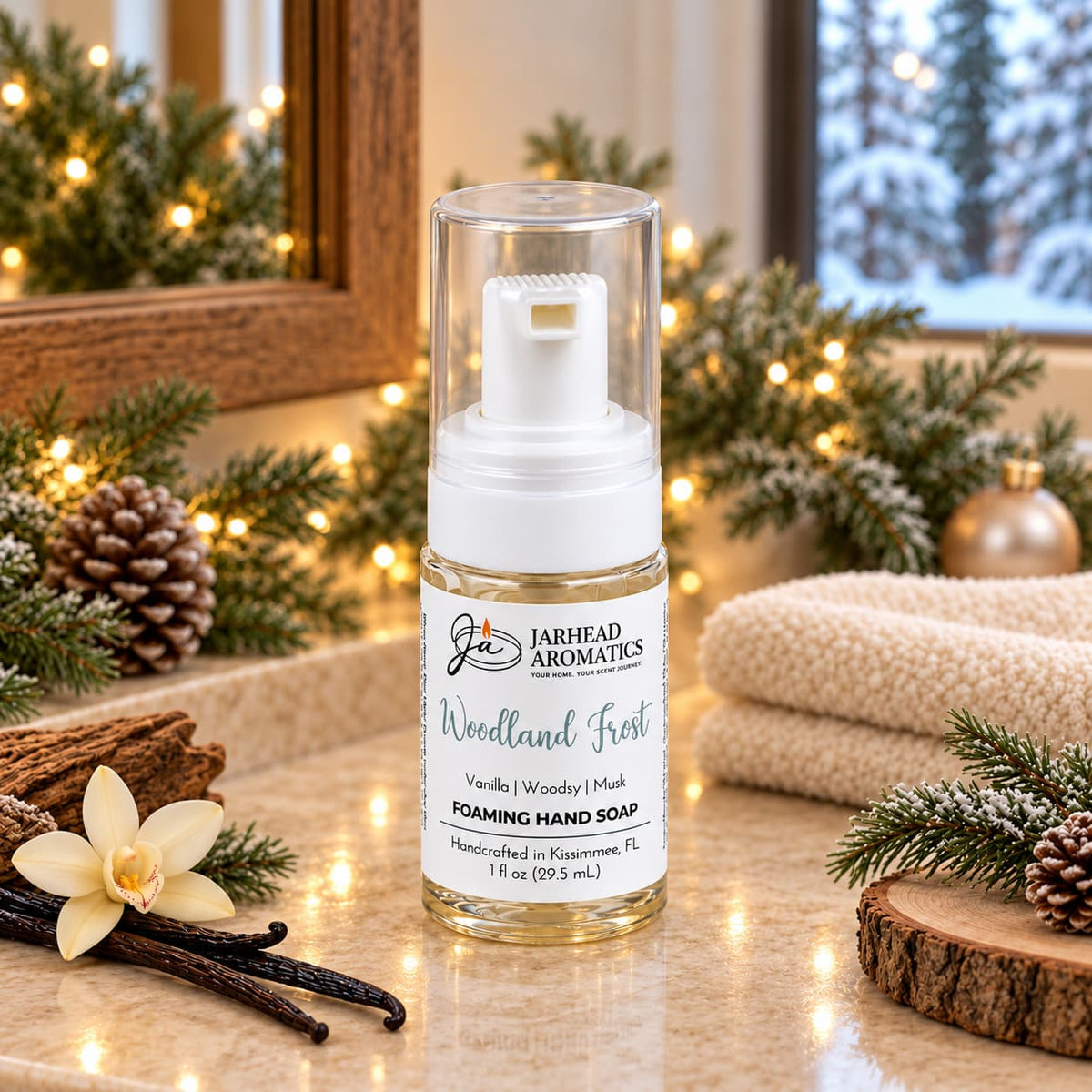 A bottle of Woodland Frost Handmade Foaming Hand Soap with a clear cap, placed on a counter decorated with pine branches, pinecones, and a vanilla flower.