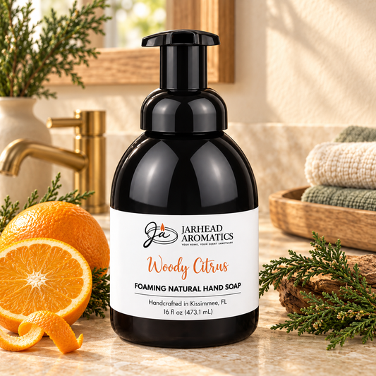 Black foaming soap dispenser of Woody Citrus Handmade Foaming Natural Hand Soap | Sweet Orange & Cypress with a label featuring an orange slice and sprig of greenery on a bathroom counter.