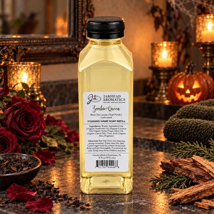 A clear bottle of Zombie Queen Handmade Foaming Hand Soap | Black Tea, Rose Petals & Cedarwood, surrounded by red roses, loose tea leaves, cedar wood chips, and a jack-o-lantern.